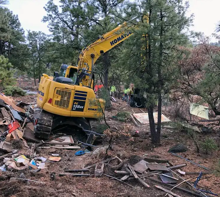 Construction workers and an excavator removing debris from a demolished structure.