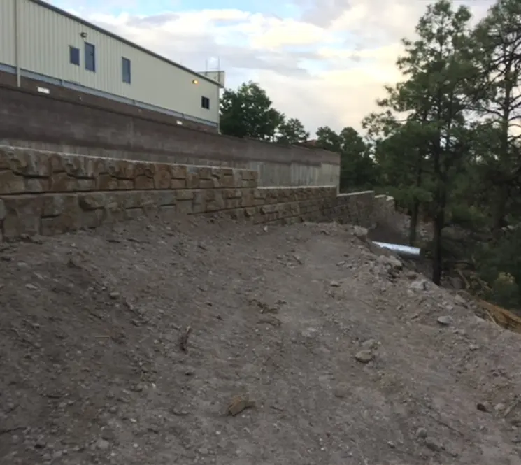 A dirt pathway leading up to a newly constructed retaining wall behind a commercial building.