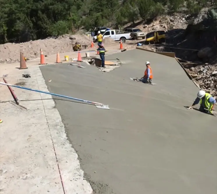 Construction workers smoothing freshly poured concrete on a sloped roadway.