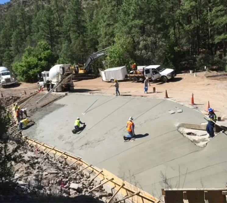 A team of workers using tools to level and finish a large concrete pavement section.
