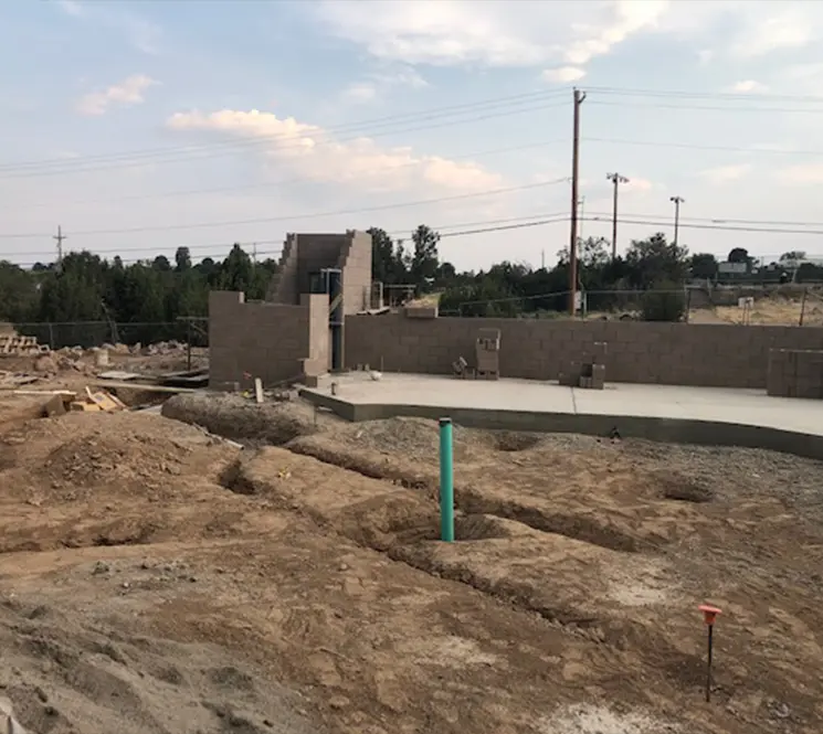 An active construction site featuring underground utility installation and foundation preparation.