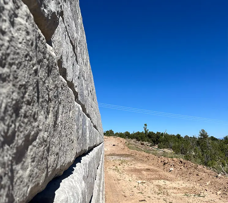 A side-angle close-up of a concrete block retaining wall with a dirt path alongside it.
