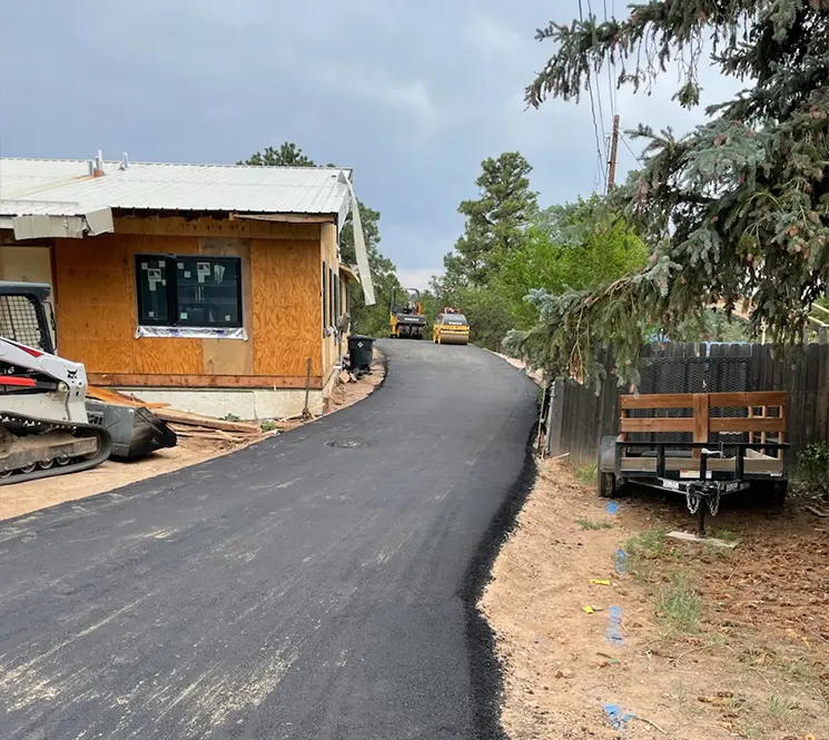 Newly laid asphalt road leading uphill with construction vehicles in the background.
