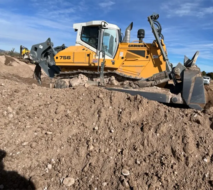 A large yellow Liebherr bulldozer moving a pile of dirt at a construction site under a clear blue sky.