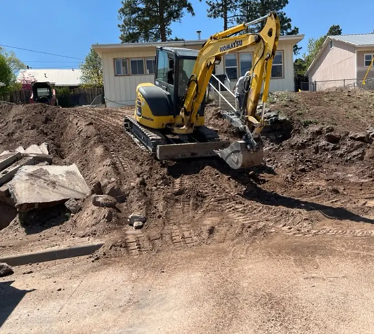 A Komatsu mini excavator working on a residential site, clearing dirt and debris near a house.