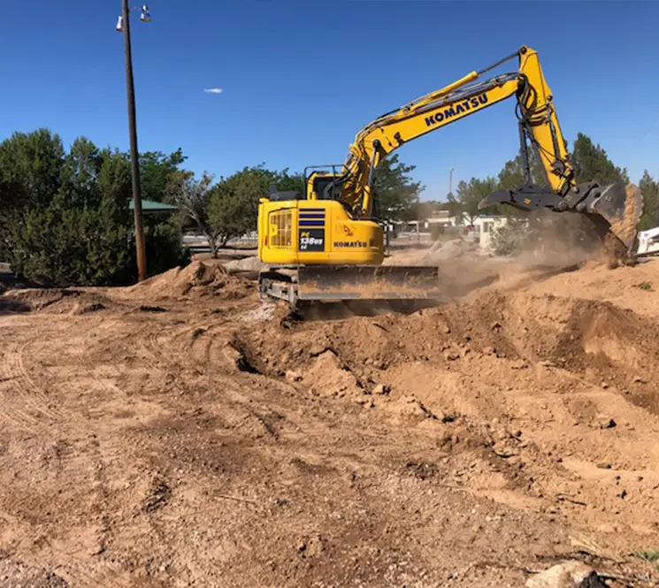A Komatsu excavator digging and moving dirt at a construction site surrounded by trees.