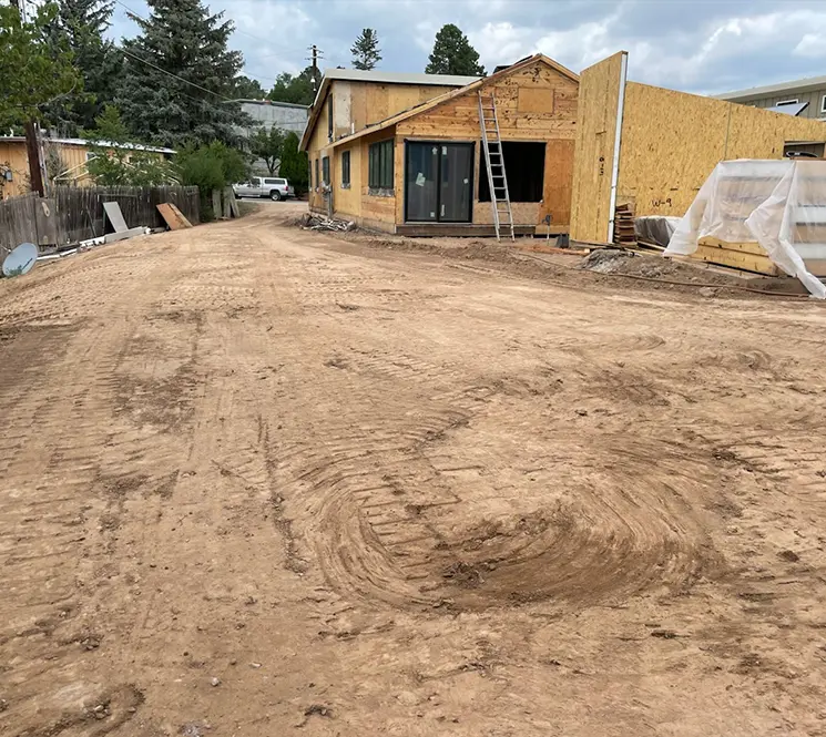 A dirt road under development in front of a partially constructed house with exposed wood framing.