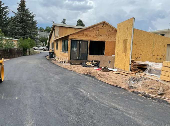Freshly paved residential road leading to a partially constructed house with plywood siding and open framing.