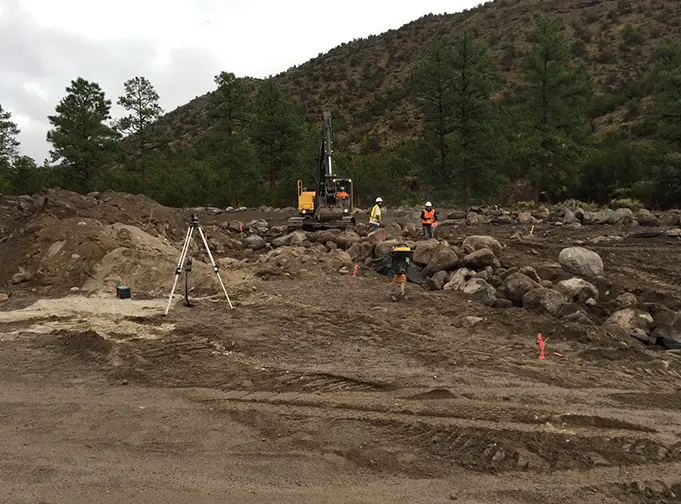Construction crew using heavy machinery to move large rocks and prepare a site for development in a mountainous area.